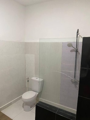 Un baño pequeño y moderno, con inodoro, cabina de ducha de vidrio y lavamanos negro.