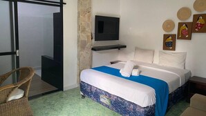 A hotel room with a bed, a television, a wicker chair, and a sliding glass door. - Private Room in Nusa Dua 300 Meters From Beach (Nusa Dua)