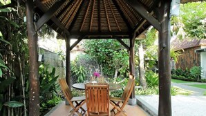 A covered outdoor seating area with a table and chairs, surrounded by greenery and a stone wall. - Private Room in Nusa Dua 300 Meters From Beach (Nusa Dua)