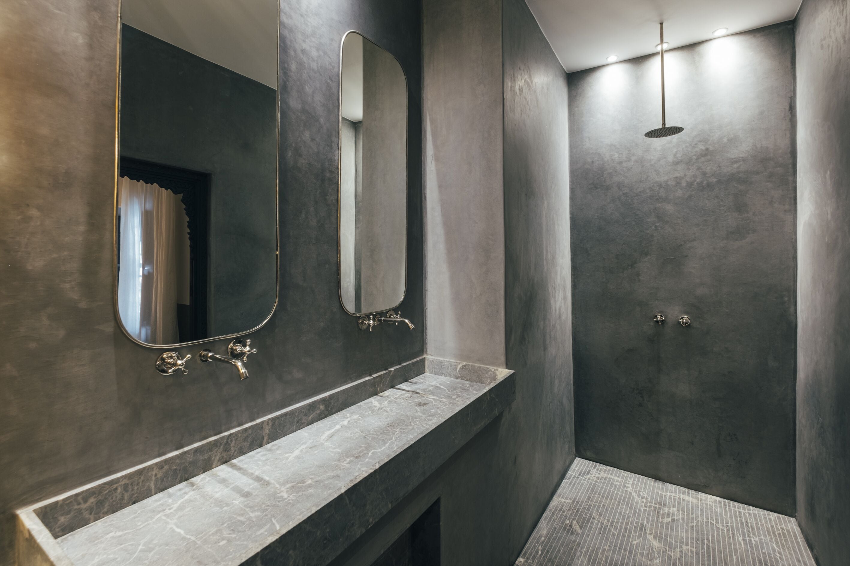 A modern bathroom with a marble sink, two mirrors, and a shower area.