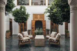 Une cour avec deux chaises en bois, une table centrale et des plantes en pot.