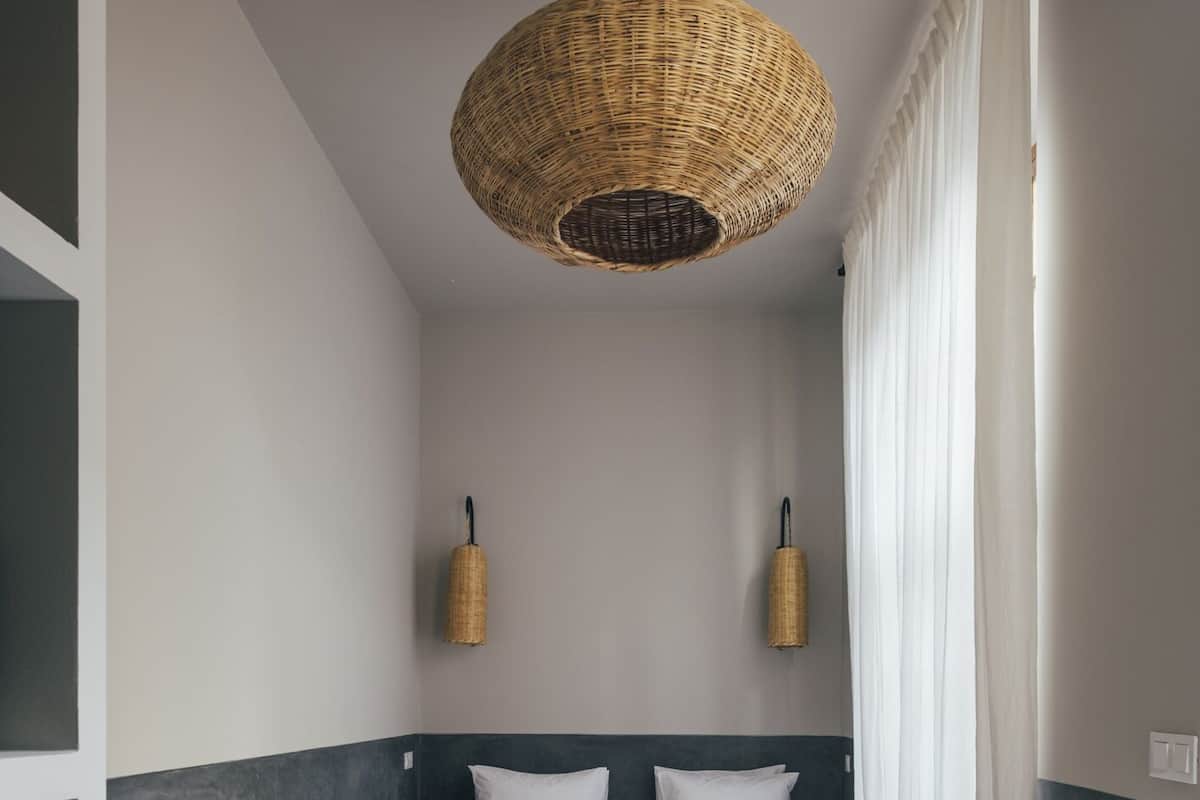 Un dormitorio con una cama, dos lámparas de pared, una silla y una lámpara de techo tejida.