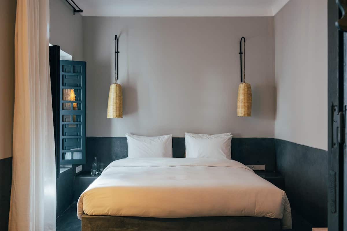 Una cama bien hecha con sábanas blancas, dos mesitas de noche y una lámpara de pared.
