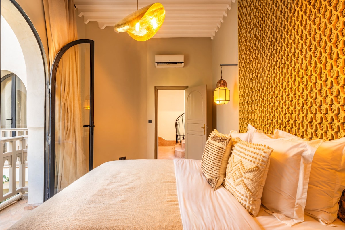 A hotel room with a bed, a mirror, an air conditioning unit, a door, and a patterned wall.