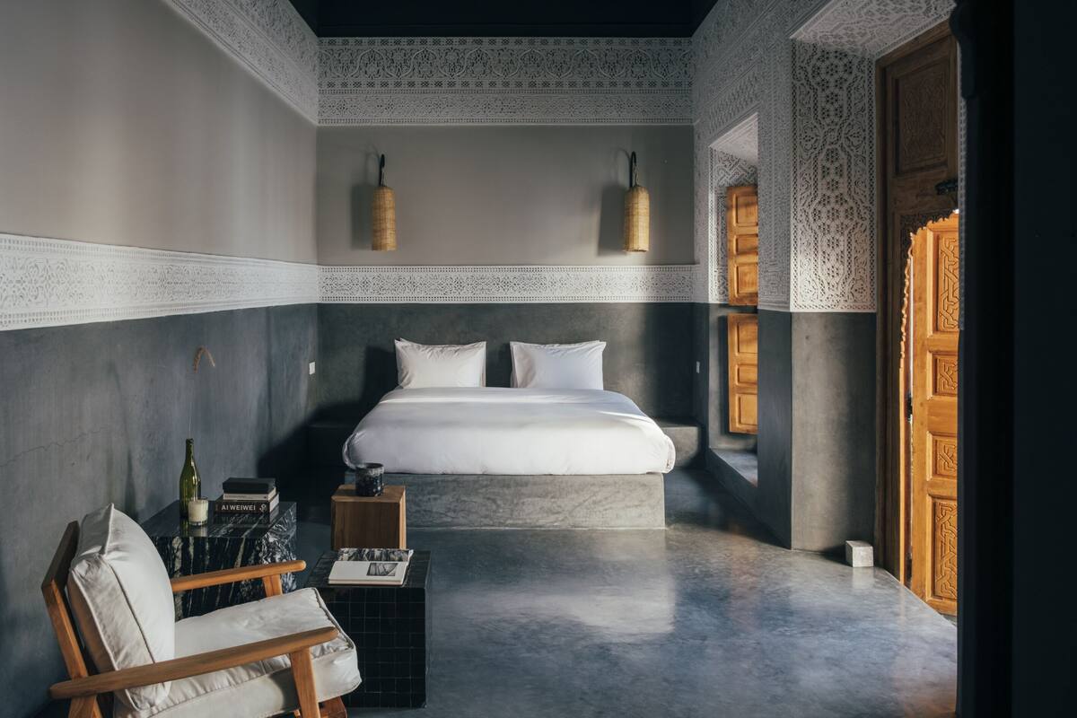 Un dormitorio moderno con una cama grande, una silla de madera, una mesita pequeña y un detalle decorativo en la pared.