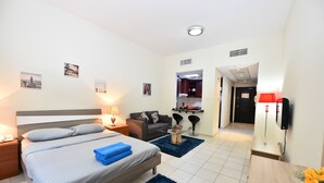 Quarto de hotel com cama, mesa de cabeceira, luminária e pequena área de cozinha.