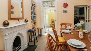 Une salle à manger avec une cheminée, une table à manger en bois dressée pour quatre personnes et une bibliothèque remplie de livres.