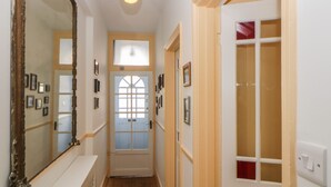 Un couloir étroit avec une porte en bois, un grand miroir et un luminaire.