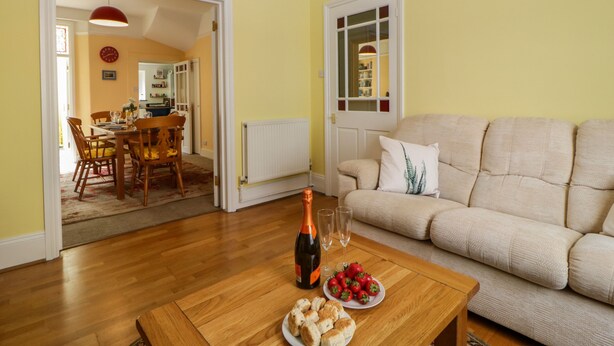Un salon avec un canapé beige, une table basse en bois sur laquelle se trouvent une bouteille de vin, des verres et des fraises.