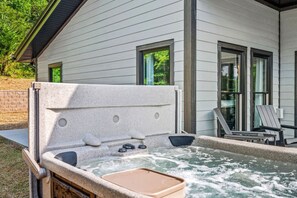 A hot tub with a stone exterior, a wooden deck, and two Adirondack chairs.