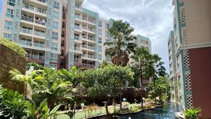 A swimming pool with a water slide, surrounded by lush greenery and tall buildings. - Grande Caribbean by PSR (Pattaya)