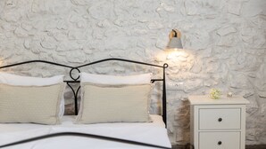 A bed with a stone wall backdrop, a bedside table with a lamp, and a small drawer unit. - Ivka in Tribalj With 4 Bedrooms and 4 Bathrooms (Vinodol)