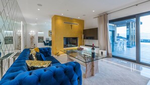 A modern living room with a blue sofa, a glass coffee table, and a fireplace. - Sara in Ka Telir With 5 Bedrooms and 5 Bathrooms (Kastelir-Labinci)
