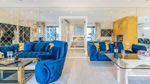 A modern living room with blue sofas, a glass coffee table, and a view into the adjacent bedroom. - Sara in Ka Telir With 5 Bedrooms and 5 Bathrooms (Kastelir-Labinci)