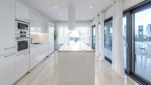 A modern kitchen with white cabinetry, a central island, and a view of the outdoors through large windows. - Sara in Ka Telir With 5 Bedrooms and 5 Bathrooms (Kastelir-Labinci)