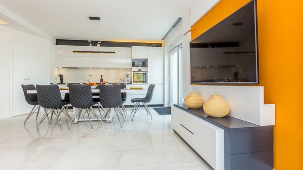 A modern kitchen with white cabinetry, a dining area with black chairs, and a large TV on a grey console. - Antonela in Malinska (Malinska-Dubasnica)