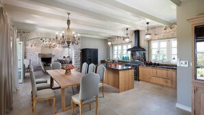 Een ruime keuken met een centraal kookeiland, een eethoek met een houten tafel en stoelen, en een stenen open haard.