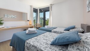 A modern hotel room with two beds, a desk, a chair, and a large window offering a view of greenery. - Frani in Pore With 4 Bedrooms and 4 Bathrooms (Porec)