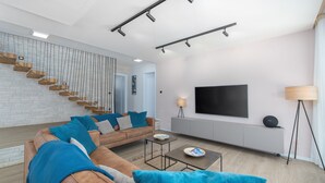 A modern living room with a sectional sofa, a flat-screen TV, a coffee table, and a staircase with built-in shelves. - Frani in Pore With 4 Bedrooms and 4 Bathrooms (Porec)