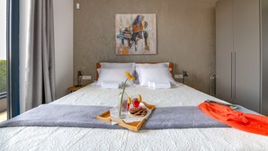 Een moderne hotelkamer met een groot bed, een schilderij aan de muur en een dienblad met snacks en een drankje.