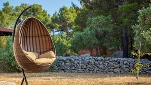 A wicker hanging chair with cushions in a garden setting.