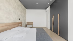 A modern bedroom with a wooden headboard, a bed with white linens, a grey throw blanket, a small wooden bench, and a wardrobe with wooden handles. - Vivas in Strani i kod Nove Vasi (Porec)