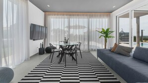 A modern living room with a sofa, a dining table with chairs, a TV mounted on the wall, and large windows with sheer curtains. - Vivas in Strani i kod Nove Vasi (Porec)