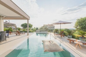 A swimming pool with lounge chairs and umbrellas, surrounded by greenery and a house in the background. - Vivas in Strani i kod Nove Vasi (Porec)