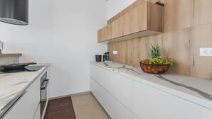 A modern kitchen with white cabinetry, a marble countertop, and a wooden wall panel. - Vivas in Strani i kod Nove Vasi (Porec)