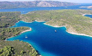An aerial view of a coastal area with clear blue waters, green hills, and boats. - Isabella Hvar in Rudina Hvar (Stari Grad)