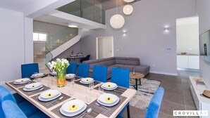 A modern dining area with a long table set for six, blue chairs, and a vase of flowers. A staircase is visible in the background. - Kastel Two in Ka tel Kambelovac (Kastela)