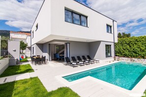 Ein modernes, zweistöckiges Haus mit Swimmingpool, Sitzgelegenheit im Freien und einem gepflegten Rasen.