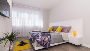 A modern bedroom with a bed, bedside table, lamp, and a potted plant. - Kastel Two in Ka tel Kambelovac (Kastela)