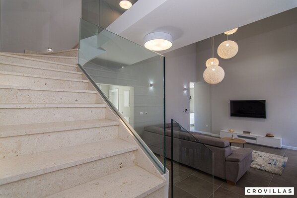 Ein modernes Interieur mit Treppe, Glasgeländern, einem grauen Sofa, einem Flachbildfernseher und einem Konsolentisch.
