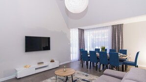 A modern living room with a flat-screen TV, a white entertainment unit, a round coffee table, and a dining area with blue chairs and a table. - Kastel Two in Ka tel Kambelovac (Kastela)