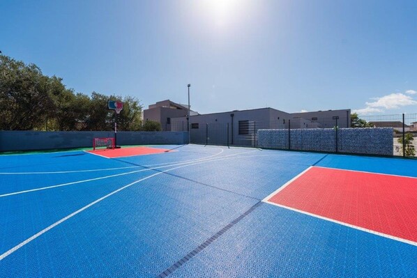 An outdoor basketball court with blue and red surfaces, a basketball hoop, and a fence. - M2 in Vir With 2 Bedrooms and 2 Bathrooms (Vir)