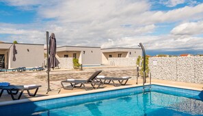 A swimming pool area with lounge chairs and umbrellas, surrounded by buildings with stone walls and a clear sky. - M2 in Vir With 2 Bedrooms and 2 Bathrooms (Vir)