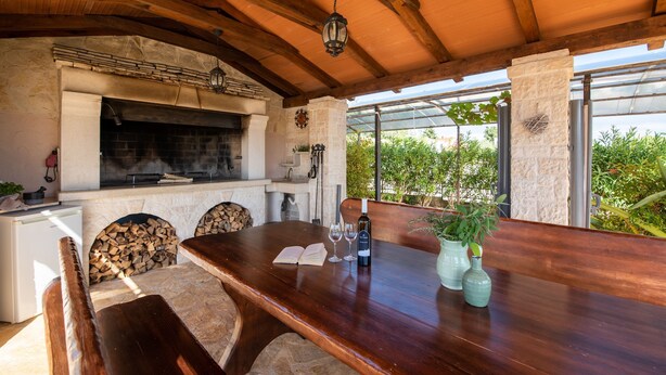 A rustic outdoor dining area with a stone fireplace, wooden beams, and a view of greenery. - Kastelir in Ka Telir (Kastelir-Labinci)