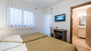 Habitación de hotel con dos camas, un escritorio, una silla, un televisor y un baño visible a través de una puerta abierta.