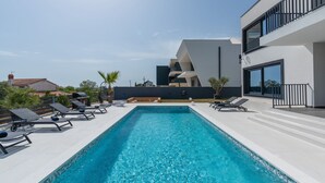 Un'area piscina moderna con lettini e una piscina blu cristallina, circondata da un edificio contemporaneo con balconi.
