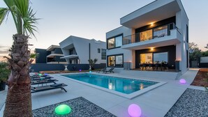 Una moderna casa a due piani con piscina, area salotto esterna e un balcone ben illuminato.