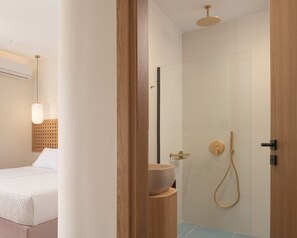 A modern bathroom with a glass shower enclosure, a wooden vanity, and a bed with a white headboard in the adjacent room. - Villa En Paraiso, a Majestic SeaView Retreat  (Maroulas)
