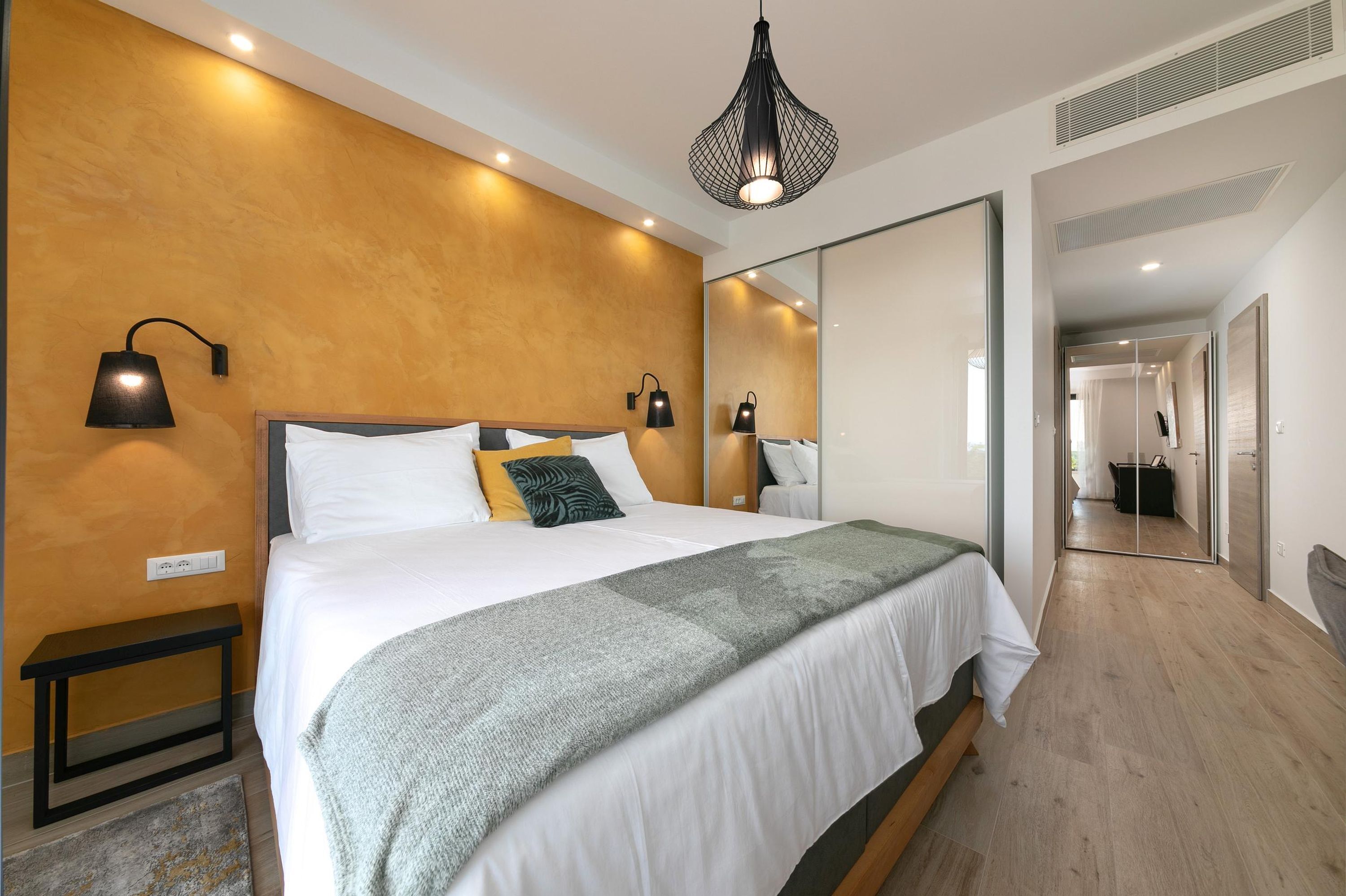 A modern bedroom with a large bed, bedside lamps, a mirror, and a wooden floor.