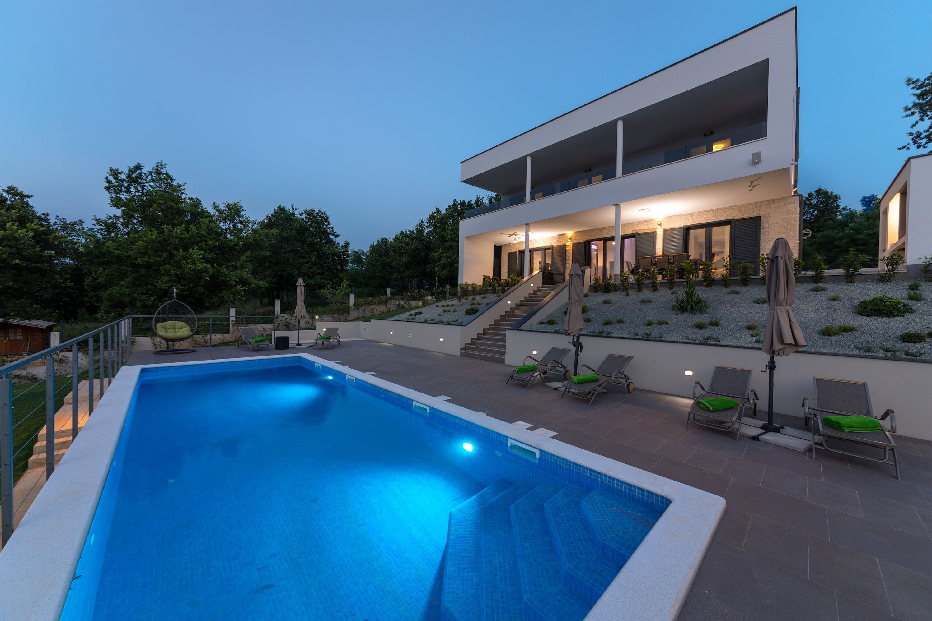 A modern two-story house with a swimming pool, outdoor seating, and a well-lit patio area.