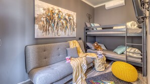 Une chambre d’enfant moderne avec un canapé gris, des lits superposés, une grande peinture abstraite et un téléviseur.