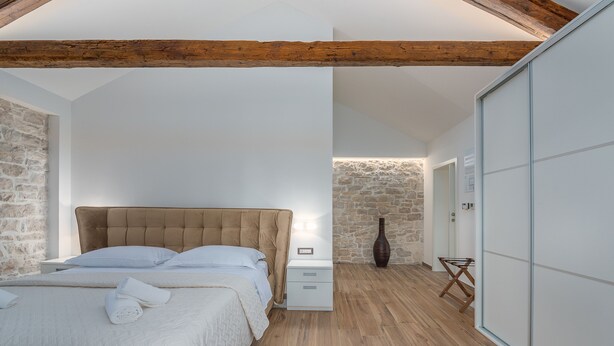 A bedroom with a wooden ceiling, stone walls, a bed with white linens, a bedside table, and a wardrobe. - Fiorini in Fiorini Brtonigla (Brtonigla)
