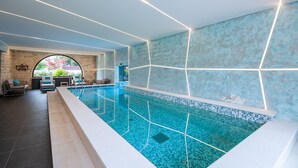 A modern indoor swimming pool with geometric lighting, stone walls, and a view of greenery outside. - Fiorini in Fiorini Brtonigla (Brtonigla)