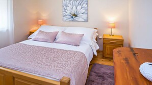 A neatly arranged bedroom with a large bed, two bedside tables with lamps, a wooden nightstand, and a wooden table. - Ognjistar in Zmijavci (Zmijavci)