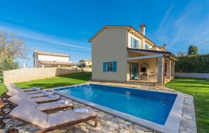Une maison à deux étages avec une piscine, des murs en pierre et un patio équipé de chaises longues.