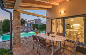 Une terrasse extérieure avec une piscine, des piliers en pierre et un espace repas comprenant des chaises et une table.